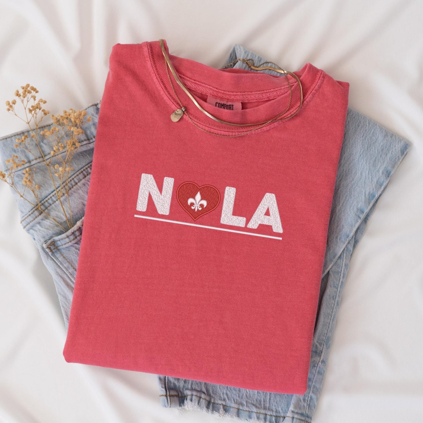 a t - shirt that says nola on it next to a pair of jeans