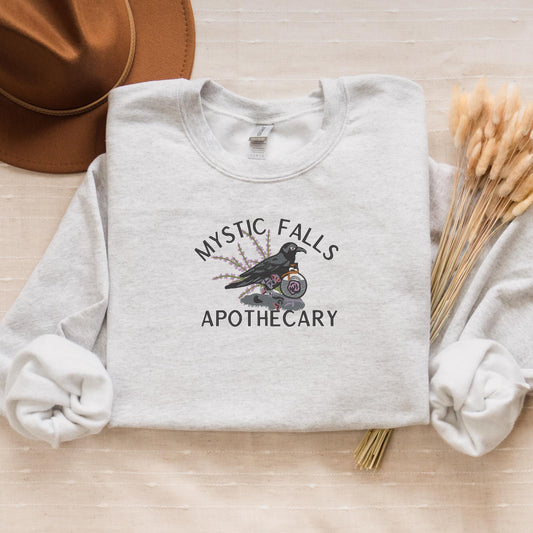 a t - shirt that says mystic falls apothecary next to a hat
