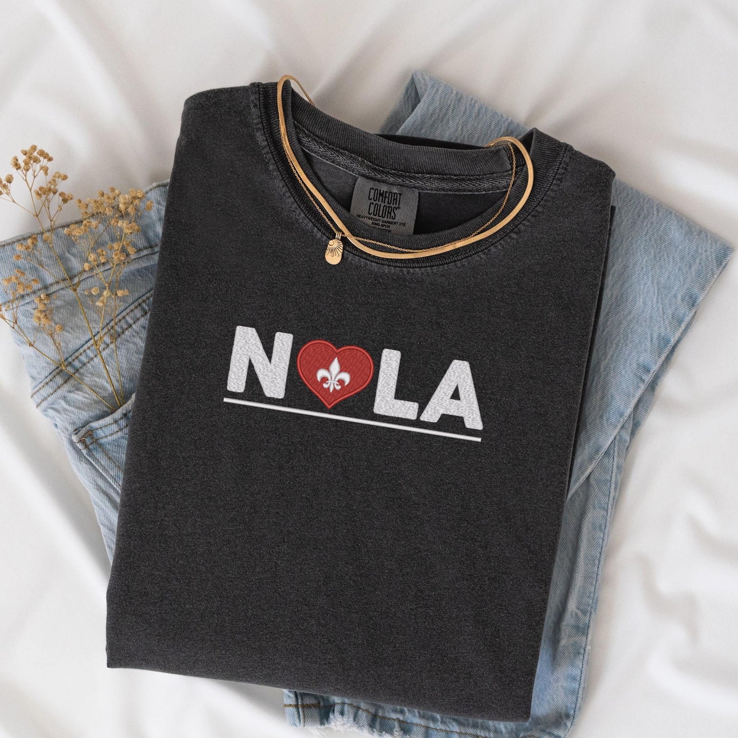 a black t - shirt with a heart and the word nola printed on it