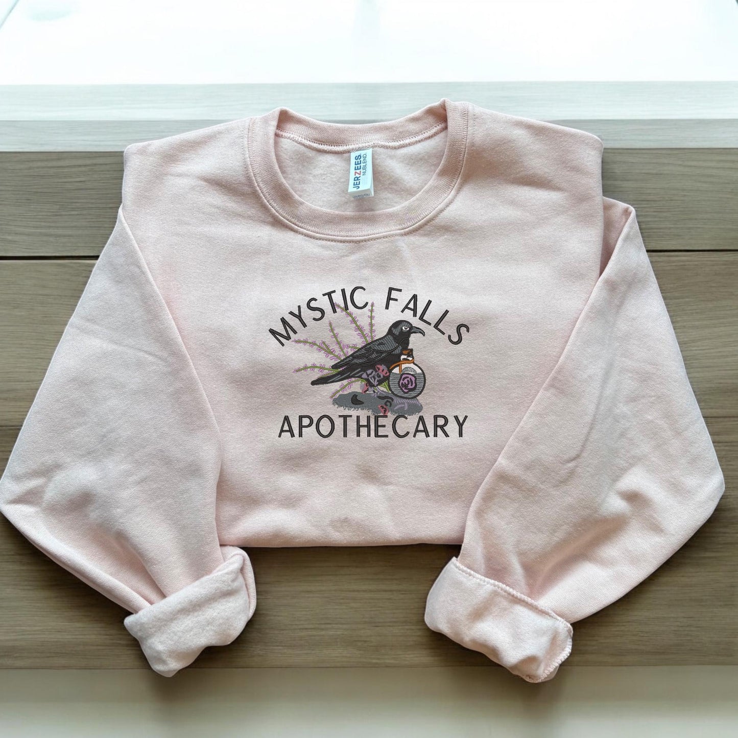 a pink sweatshirt that says mystic falls apothecary
